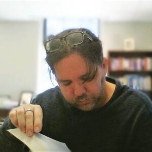 A close up of Brandon Hobson reading in a library with his glasses atop his head