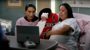 A male and female Native couple hold a baby in a red cradleboard in a screenshot from the television show Grey's Anatomy