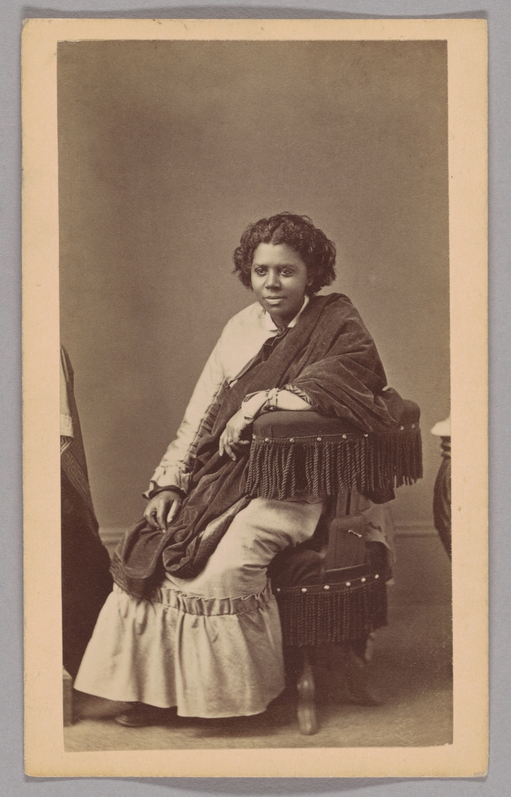 19th-century studio portrait of the sculptor featured in Edmonia Lewis: Said in Stone, seated in a long dress and shawl beside an upholstered chair against a plain backdrop