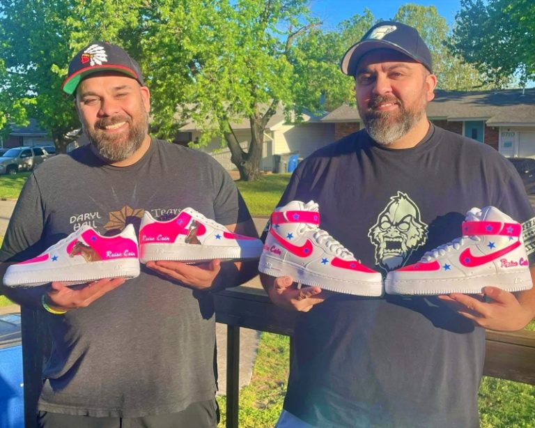 Brothers Chris and Jeremy Thompson stand outdoors holding matching custom Nike sneakers with pink, blue, and star designs, showcasing their collaborative work through Semurai Designs.