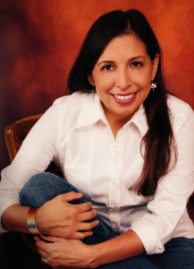 Wendy Mahsetky-Poolaw smiling in a white blouse during a seated portrait.